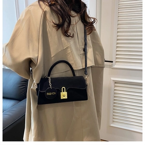 Détail du sac bandoulière noir avec boucle dorée et charm de mode sur manteau beige