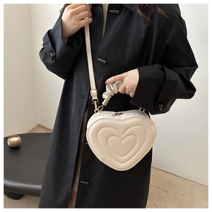 White heart-shaped crossbody bag with pleated handle shown on a black winter coat