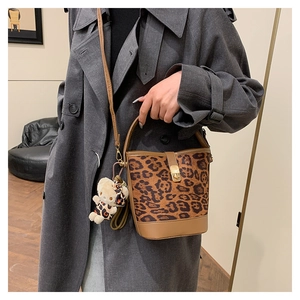 Close-up of leopard print bucket bag with brown leather strap and plush bear charm