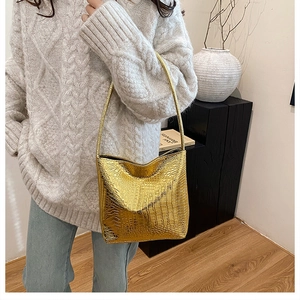 Detailed view of a gold crocodile pattern bucket bag styled with a white knit sweater