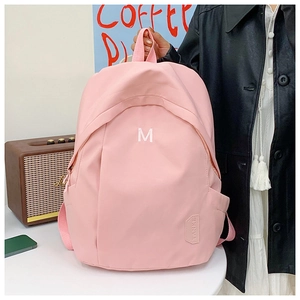 Close-up of light pink nylon backpack featuring white M embroidery and decorative patch