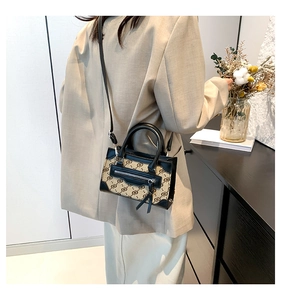 Detail of a vintage pattern canvas handbag with black leather trim worn by a model