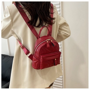 Close-up of a red quilted mini backpack with gold zippers worn over a beige blazer