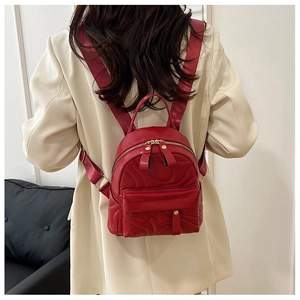 Detailed view of bright red mini backpack with wavy quilted pattern and gold zipper details