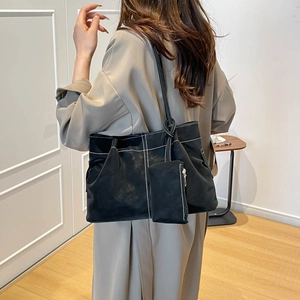 Minimalist black suede tote bag with contrast stitching and small pouch on a model