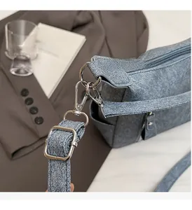 Detail of high-quality silver metallic buckle and adjustable strap on a gray denim bag