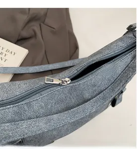 Close-up of a smooth silver zipper on a gray matte textured crossbody commuter tote bag