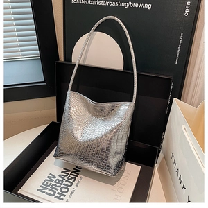 Detail of silver crocodile pattern bucket bag with metallic glossy finish on a black box