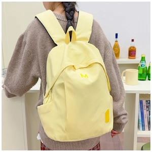 Detail view of bright yellow water-resistant school backpack with letter M embroidery