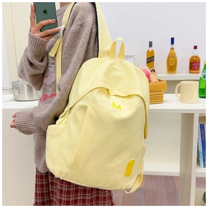 Detail of a bright lemon yellow nylon backpack with a bold yellow letter M decoration