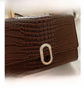 Close-up of brown faux crocodile leather texture and golden oval metal lock on handbag