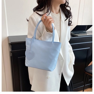 Detail shot of a light blue nylon tote bag with heart charm carried by a model