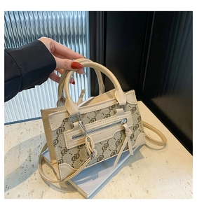 Detail of beige monogram shoulder bag featuring dual handles and metallic zipper accents