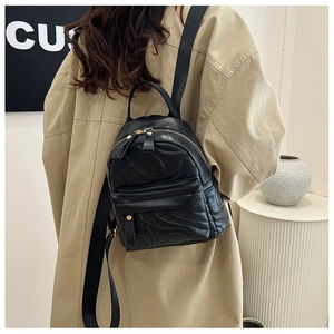 Close-up of black quilted mini backpack with gold hardware worn by a person