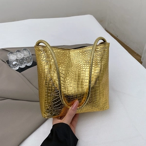 Golden tote bag with crocodile texture and long top handles in a lifestyle setting