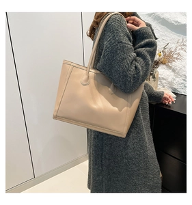 Beigefarbene Tragetasche aus Kunstleder am Model getragen in minimalistischem Interieur