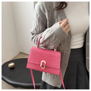 Detail of hot pink crocodile pattern crossbody bag with a golden oval lock and gray cardigan