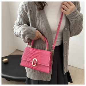Detail of rose red crocodile pattern handbag with gold clasp and long shoulder strap