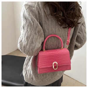 Detail of rose pink crocodile embossed handbag with gold buckle shown on a model