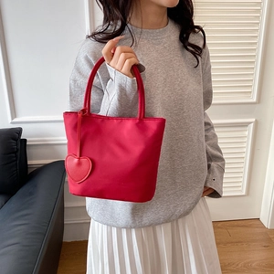 Minimalist red nylon tote bag with heart pendant accessory shown in lifestyle setting