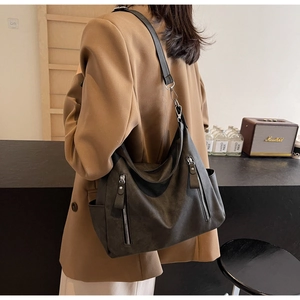 Side view of a large black matte hobo bag worn by a model in a cozy cafe setting