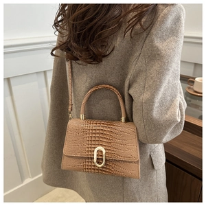 Close-up of crocodile pattern leather texture and gold metal buckle on a shoulder bag