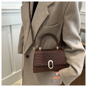 Detail of coffee brown crocodile pattern leather handbag with gold oval clasp buckle