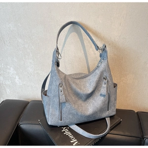 Detail of grey matte shoulder bag showing vertical zippers and texture on a leather bench