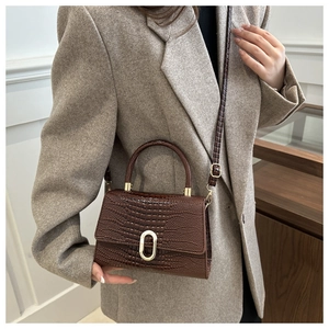 Detail of dark brown croc-embossed handbag with gold hardware on a grey blazer