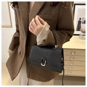Detail of black crocodile texture handbag with golden U-shaped buckle on brown suit