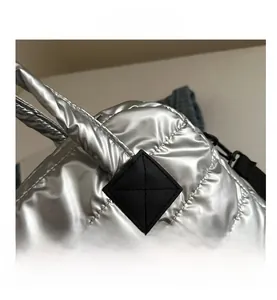 Détail du sac matelassé argenté avec écusson en cuir noir et finition métallique brillante