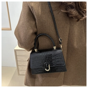 Detailed view of black crocodile pattern crossbody bag styled with a brown winter coat