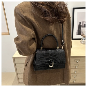 Detail view of black crocodile pattern faux leather handbag with golden oval lock clasp