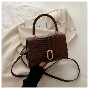 Close-up of dark brown crocodile embossed leather texture and oval metal buckle detail