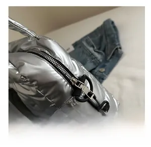 Détail de la fermeture éclair noire lisse et du tissu matelassé métallisé du sac argenté