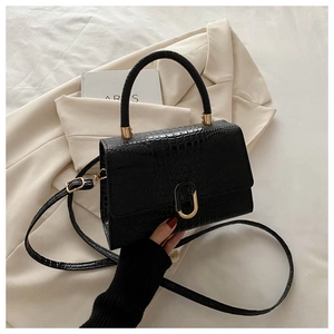 Detail of black crocodile texture handbag with golden U-shaped lock on white blazer