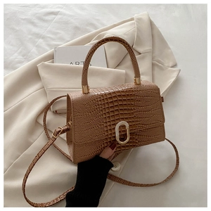 Detail of a brown crocodile pattern trapezoid handbag with a golden oval buckle and strap