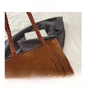 Close-up of brown suede bucket bag with braided handle and long decorative fringe details
