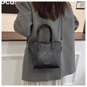 Detailed view of black matte leather bucket bag featuring gold fashion lettering and strap