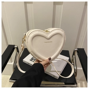 Detail of a beige heart-shaped crossbody bag with gold metal zipper and leather texture