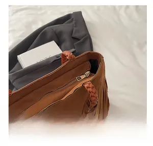 Detail of smooth metal zipper and woven handle on brown suede fringe tote bag