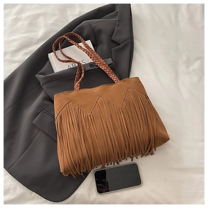 Detailed view of bohemian suede tassel tote bag with braided handles on white fabric