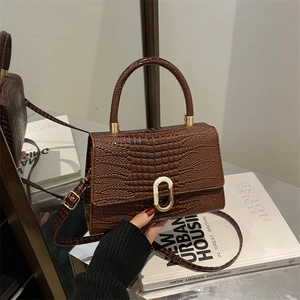 Dark brown faux crocodile leather handbag with metal buckle and shoulder strap in urban setting