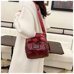 Detail of burgundy quilted down crossbody bag featuring a fashion label and wide strap