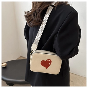 Detail of cream camera bag with red heart and patterned wide shoulder strap