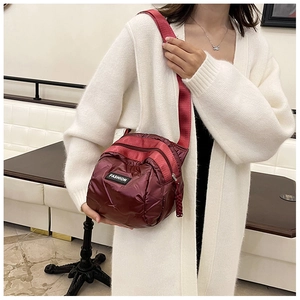 Detail of burgundy quilted puffer bag with fabric strap and fashion label on front