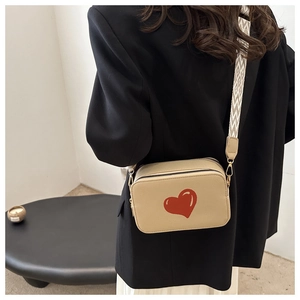 Detail of beige crossbody bag with red heart and patterned wide shoulder strap