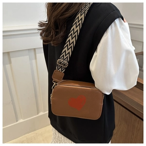 Detail of brown leather camera bag with red heart pattern and wide geometric woven strap