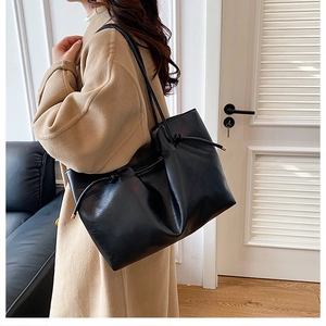 Detail einer schwarzen Leder-Tote-Bag mit Kordelzug, getragen über einem beigen Mantel