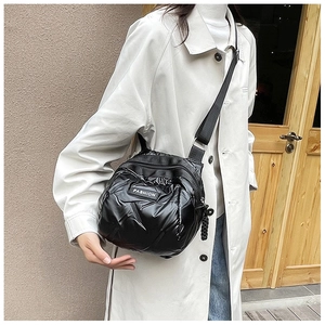 Detail of black puffer crossbody bag with glossy finish and white FASHION logo tag